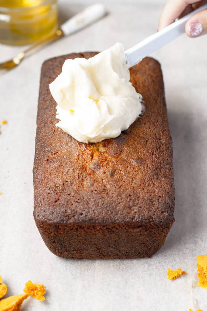 Spreading cream cheese frosting on honeycomb walnut loaf cake