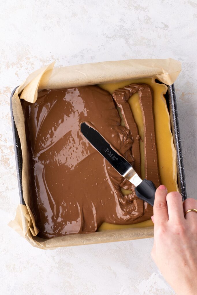 Spreading chocolate on top of caramel