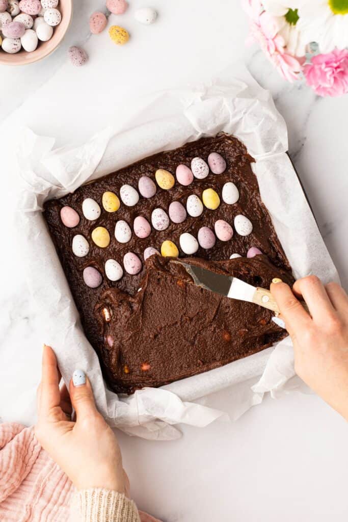 spreading brownie mixture over a layer of mini eggs