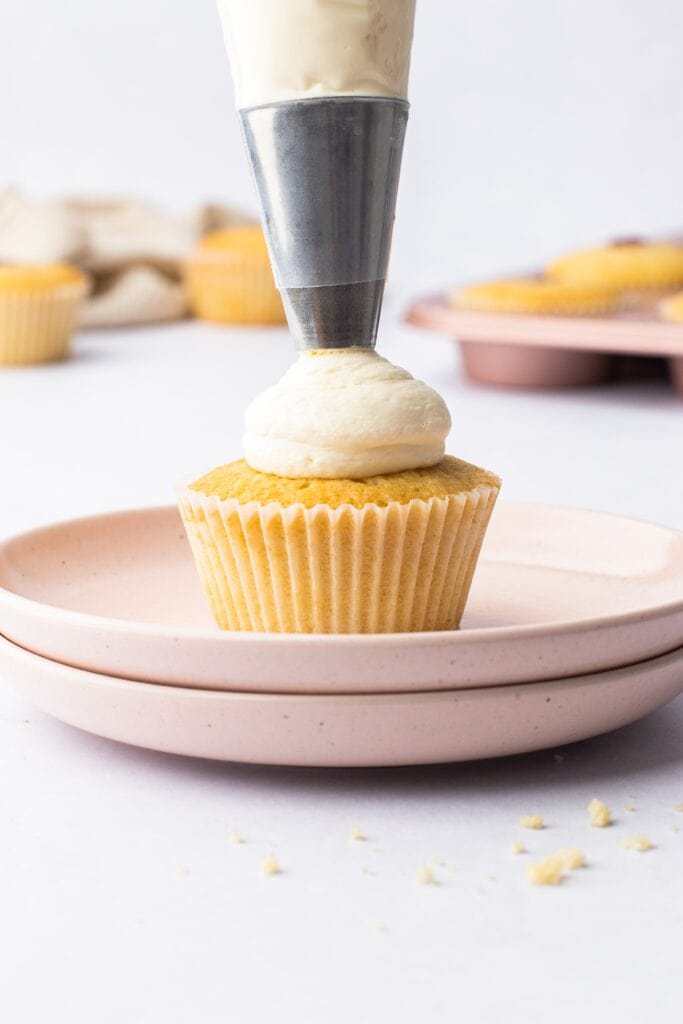 piping whipped cream on top of victoria sponge cupcakes