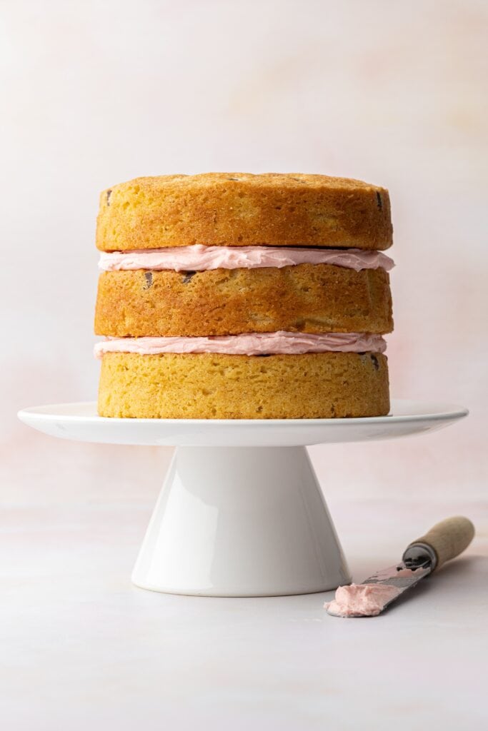 stacking the cake layers with pink vanilla buttercream