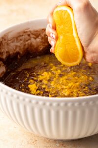 A hand squeezing an orange into a bowl of cake mix