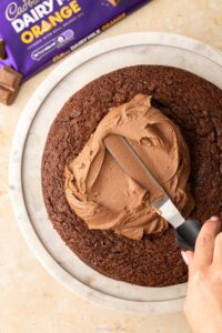 A hand spreading chocolate orange buttercream onto a cake using a palette knife