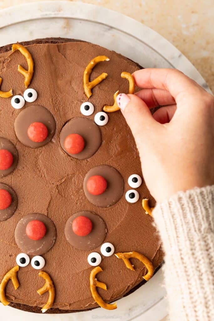 A hand putting the finishing touches to the decoration on a chocolate orange reindeer cake