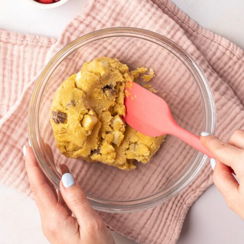 A top down view of bowl of cookie dough being mixed by someone