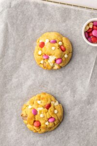 Two thick NYC style chocolate chunk cookies with red and pink Smarties as toppings