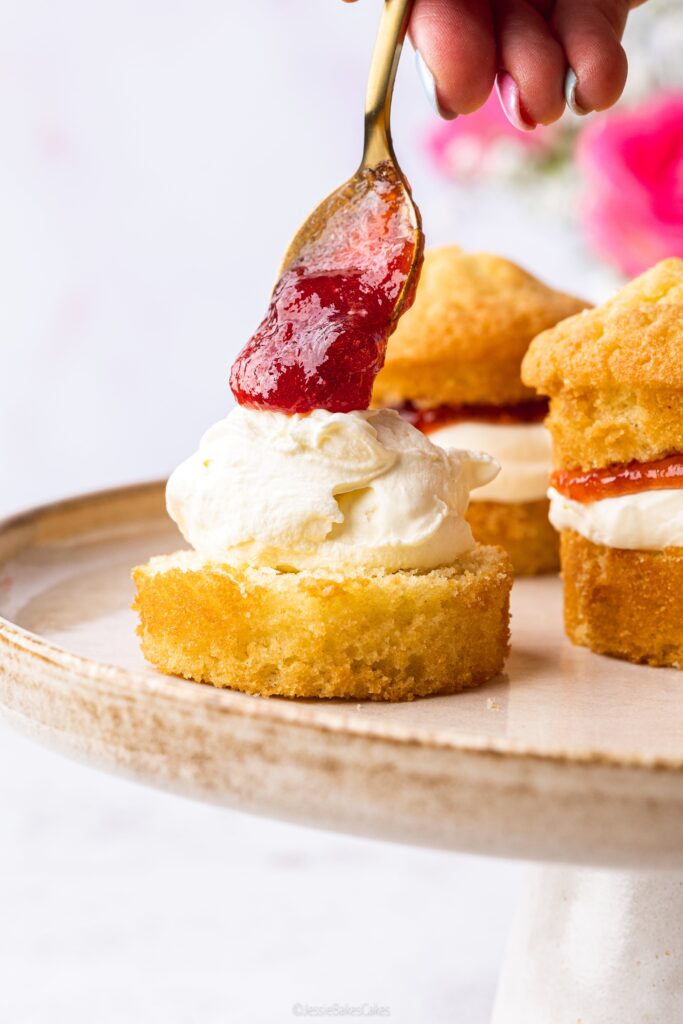 Spooning strawberry jam on top of cream and sponge cakes