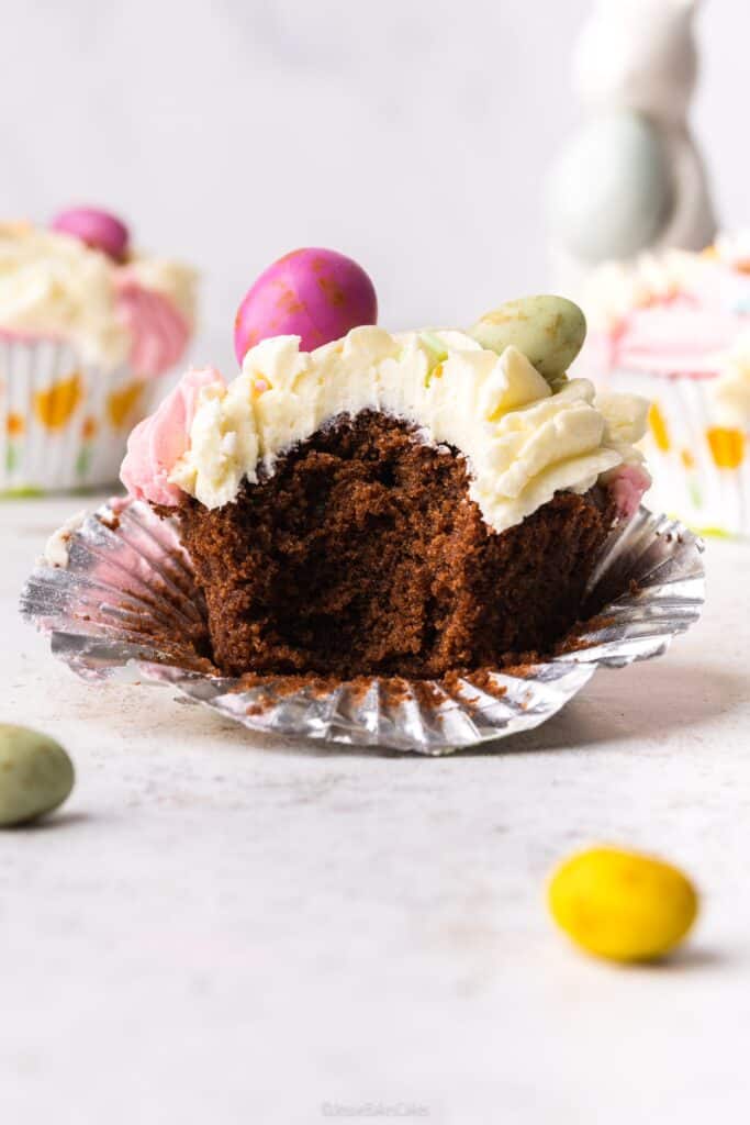 A single chocolate cupcake with a bite taken out of it, topped with vanilla buttercream and mini eggs