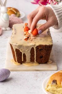 A hand adding the finishing touch to a Sticky Toffee Hot Cross Loaf Cake