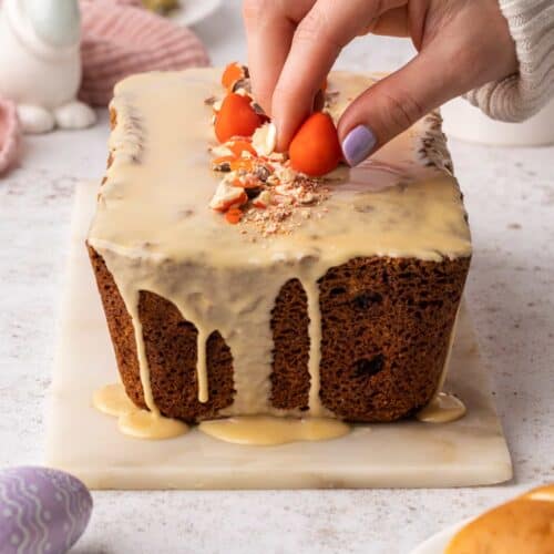 A hand adding the finishing touch to a Sticky Toffee Hot Cross Loaf Cake