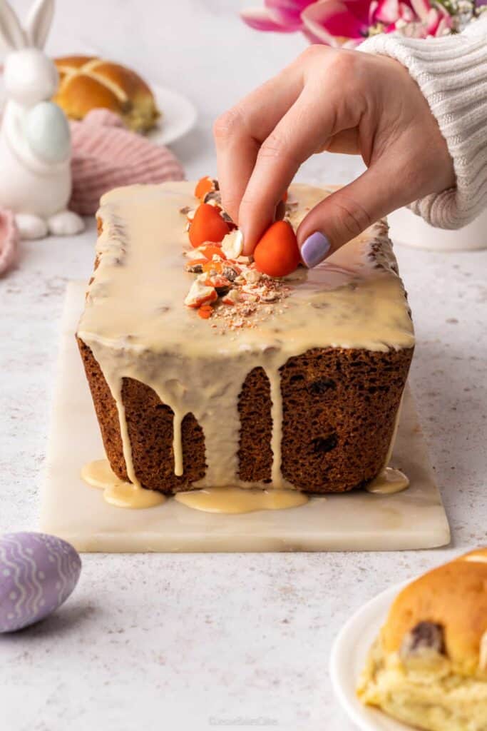 A hand adding the finishing touch to a Sticky Toffee Hot Cross Loaf Cake