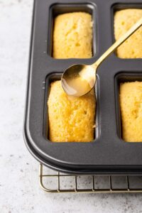 Spooning lemon drizzle onto mini lemon drizzle loaf cakes