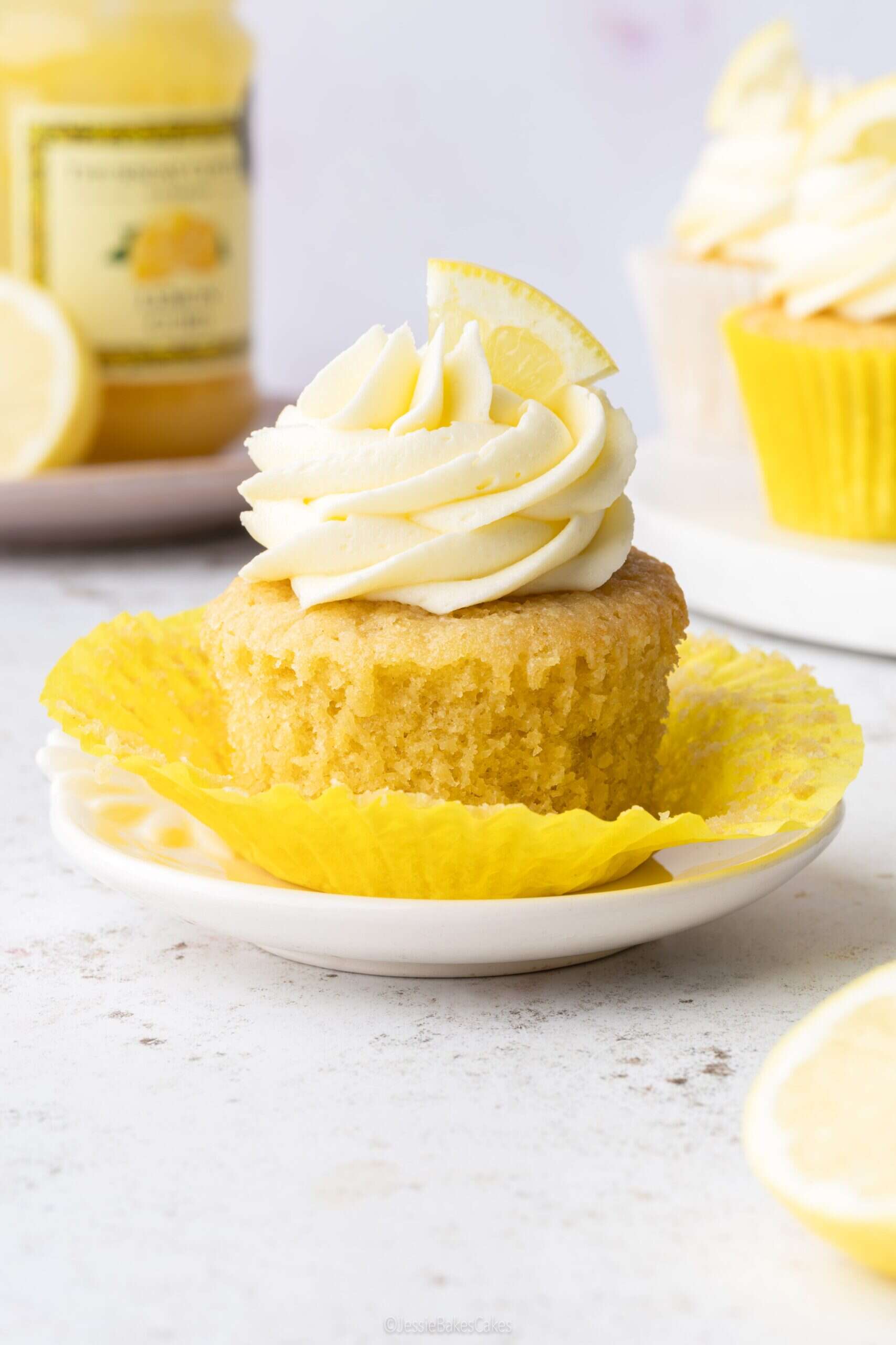 a single lemon cupcake on a small plate with a jar of lemon curd