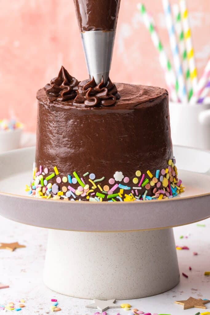 piping chocolate fudge frosting onto a mini cake