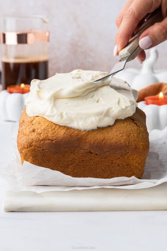 spreading maple spice cream cheese frosting on top of pumpkin cake