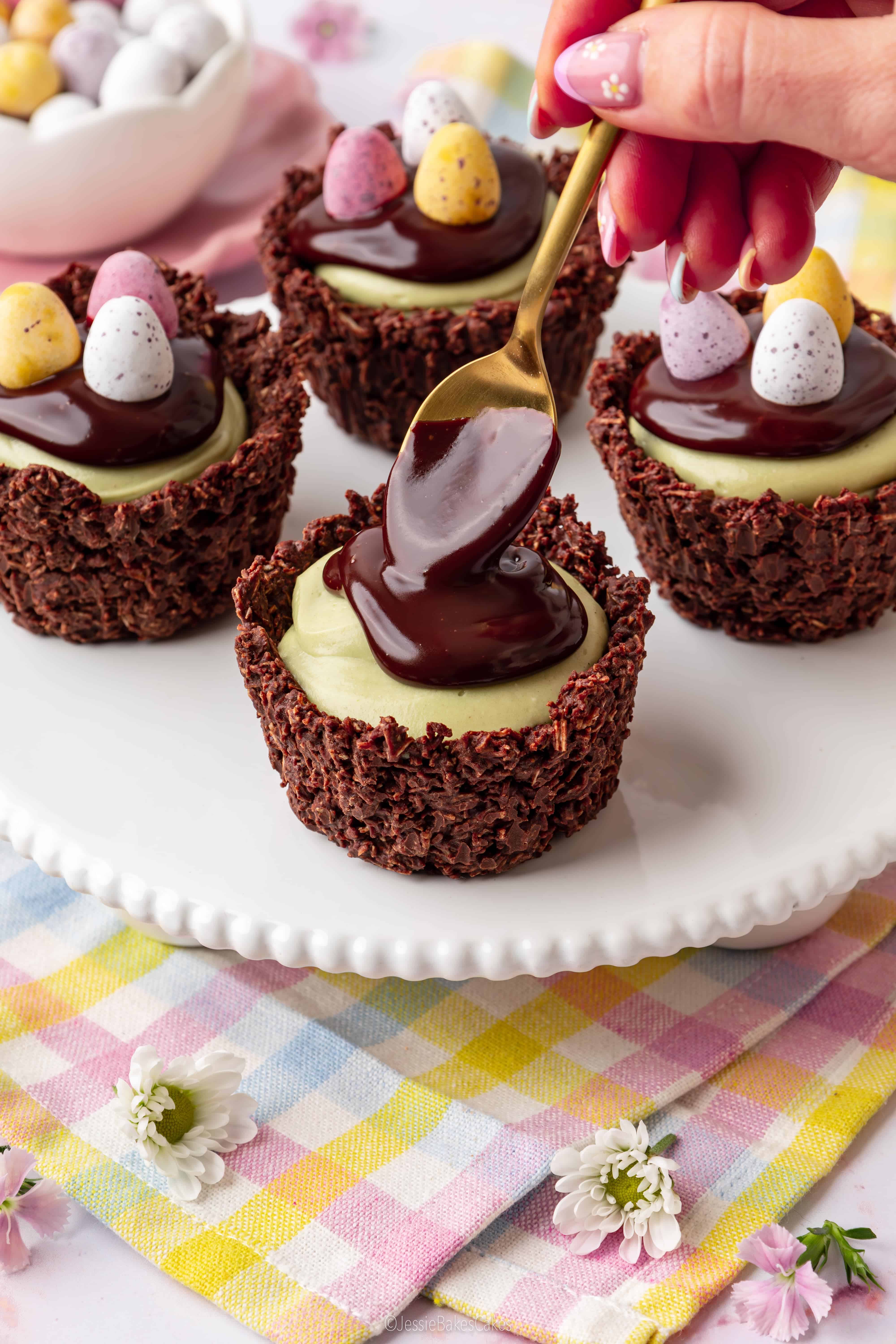 Putting chocolate ganache on top of pistachio cheesecakes