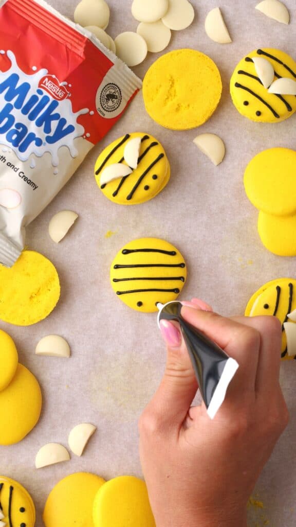 decorating bee macarons with black writing icing