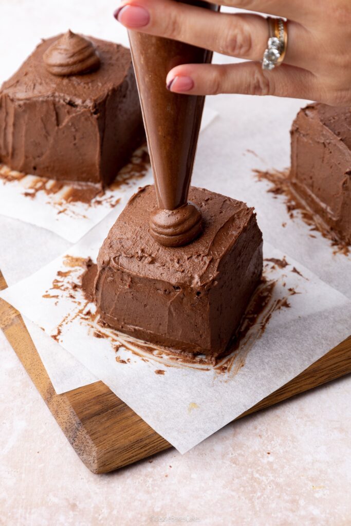 piping a dome of chocolate buttercream on top of the cakes